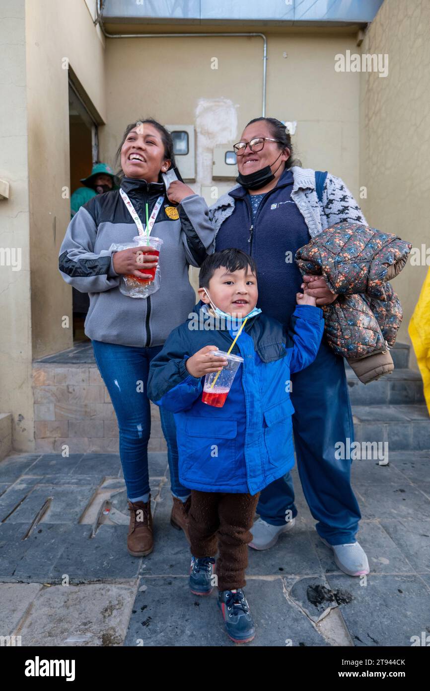 Viacha, la Paz, Bolivia – 16 agosto 2022: Donne boliviane e un ragazzo con maschere appendere in strada e bere succo Foto Stock