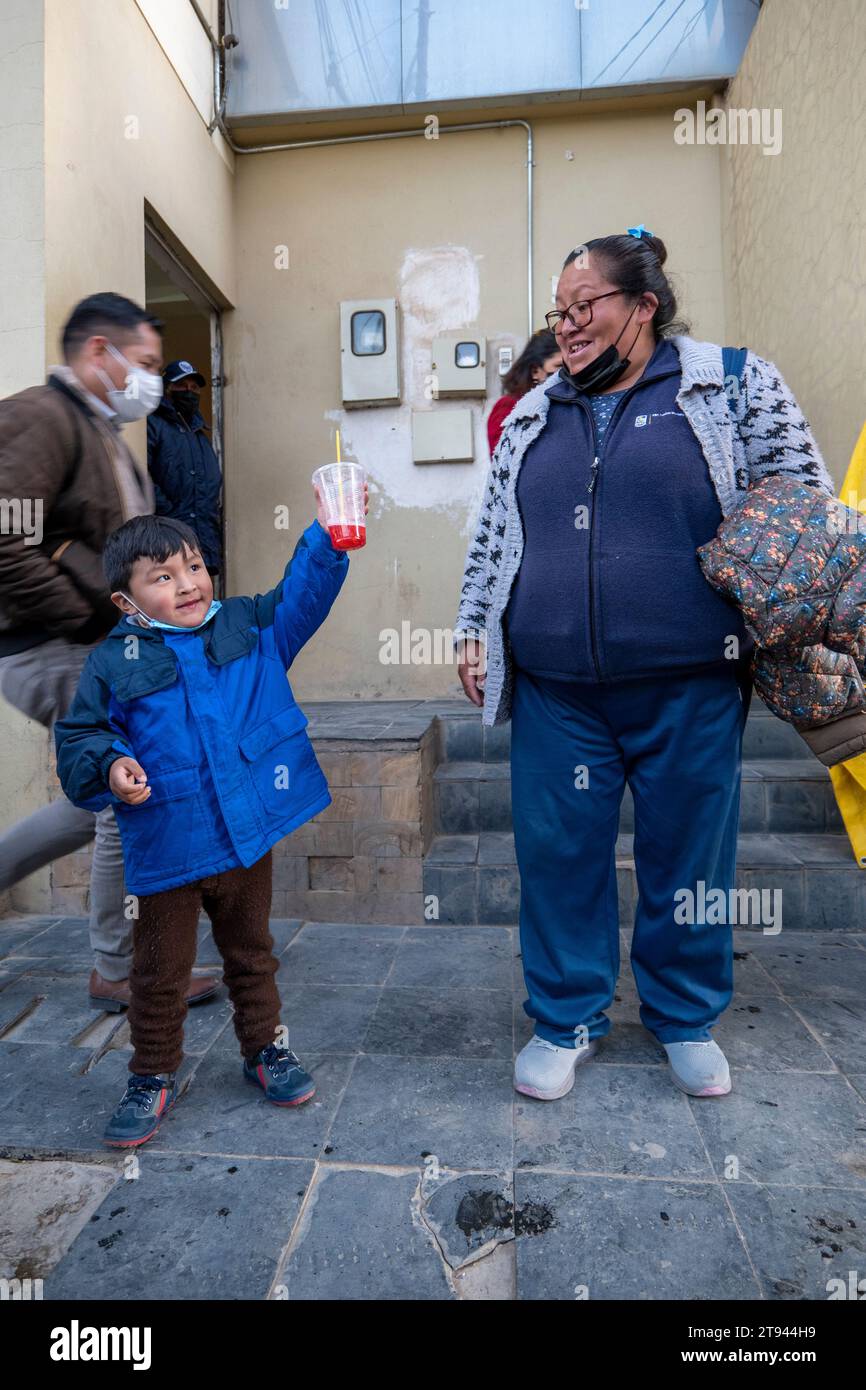 Viacha, la Paz, Bolivia – 16 agosto 2022: Donne boliviane e un ragazzo con maschere appendere in strada e bere succo Foto Stock