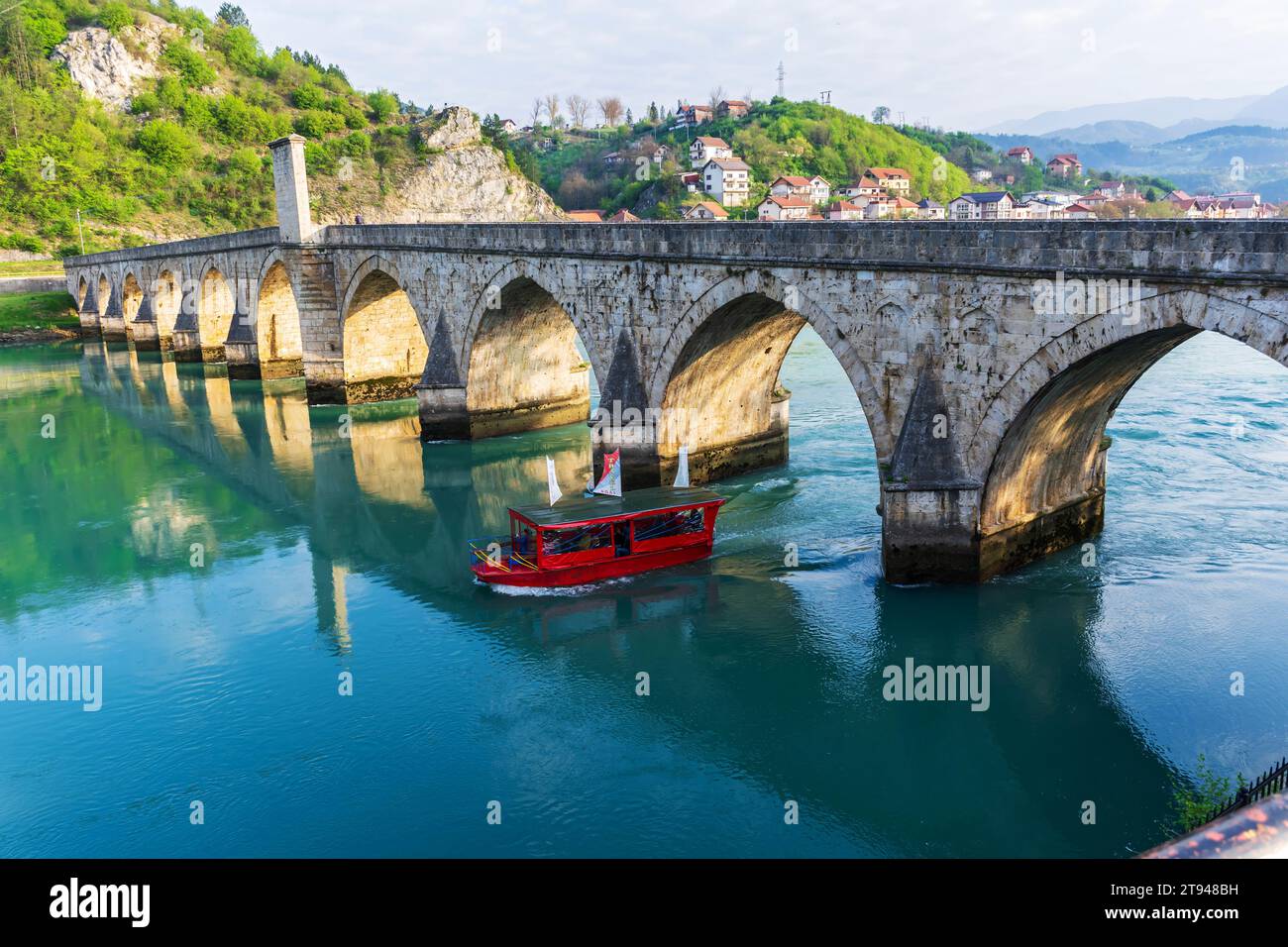 La barca turistica passa sotto il famoso ponte sul fiume Drina a Visegrad, Bosnia ed Erzegovina. Foto Stock
