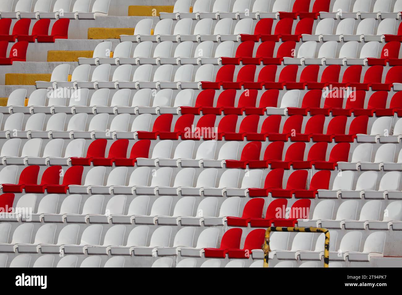 molti posti vuoti in plastica rossa e bianca nello stadio si trovano senza persone prima dell'evento sportivo Foto Stock