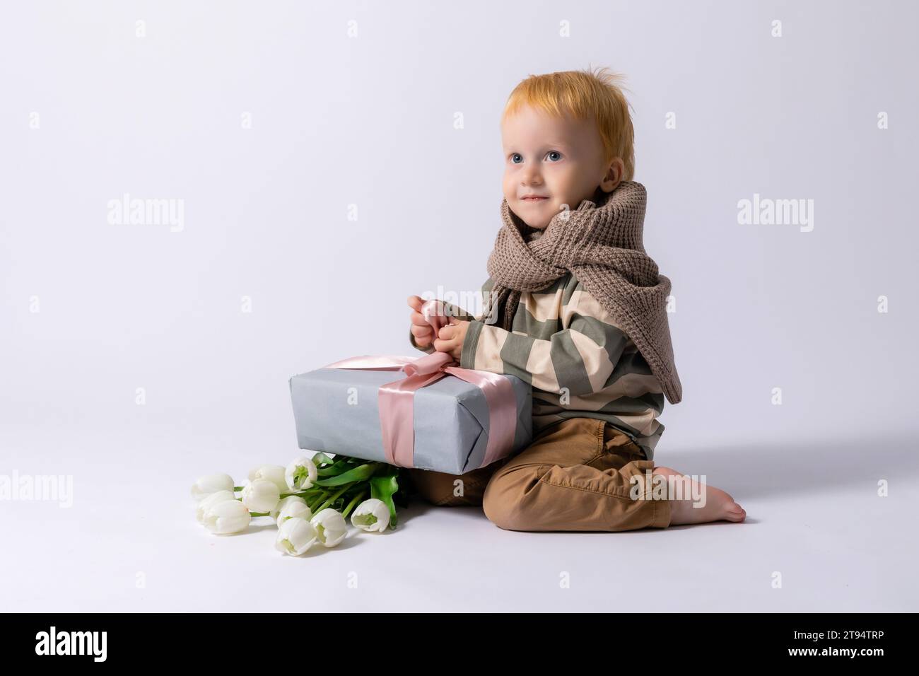 grazioso bambino di 3 anni che regge tulipani e una confezione regalo su sfondo bianco. 8 marzo, spazio per il testo. Foto Stock