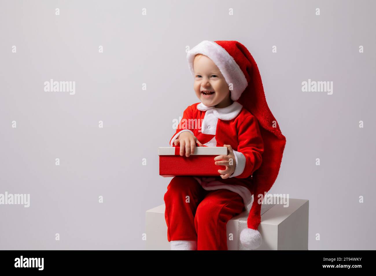 Un ragazzino biondo in costume di Babbo Natale su sfondo bianco. Foto di alta qualità Foto Stock