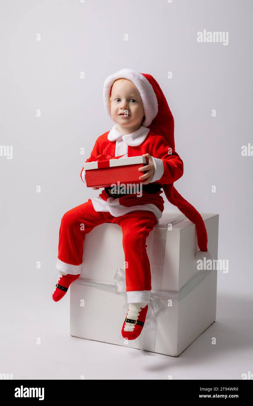 Un ragazzino biondo in costume di Babbo Natale su sfondo bianco. Foto di alta qualità Foto Stock