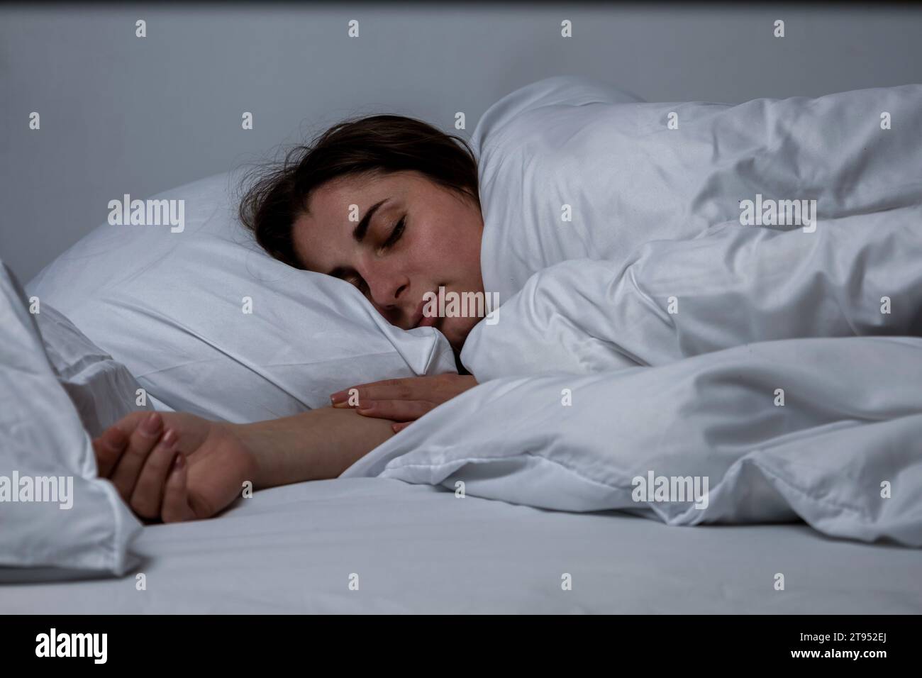 La ragazza sta dormendo in un letto con un lenzuolo bianco Foto Stock