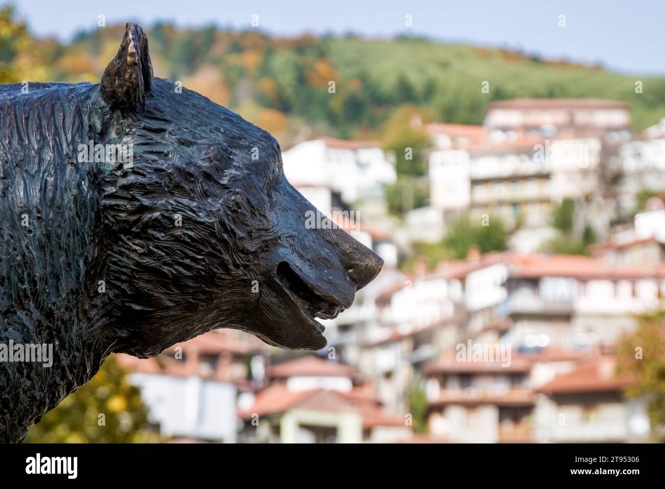 La statua di un orso madre con il tradizionale villaggio montano di Metsovo sullo sfondo, nel nord della Grecia, in Europa. Foto Stock