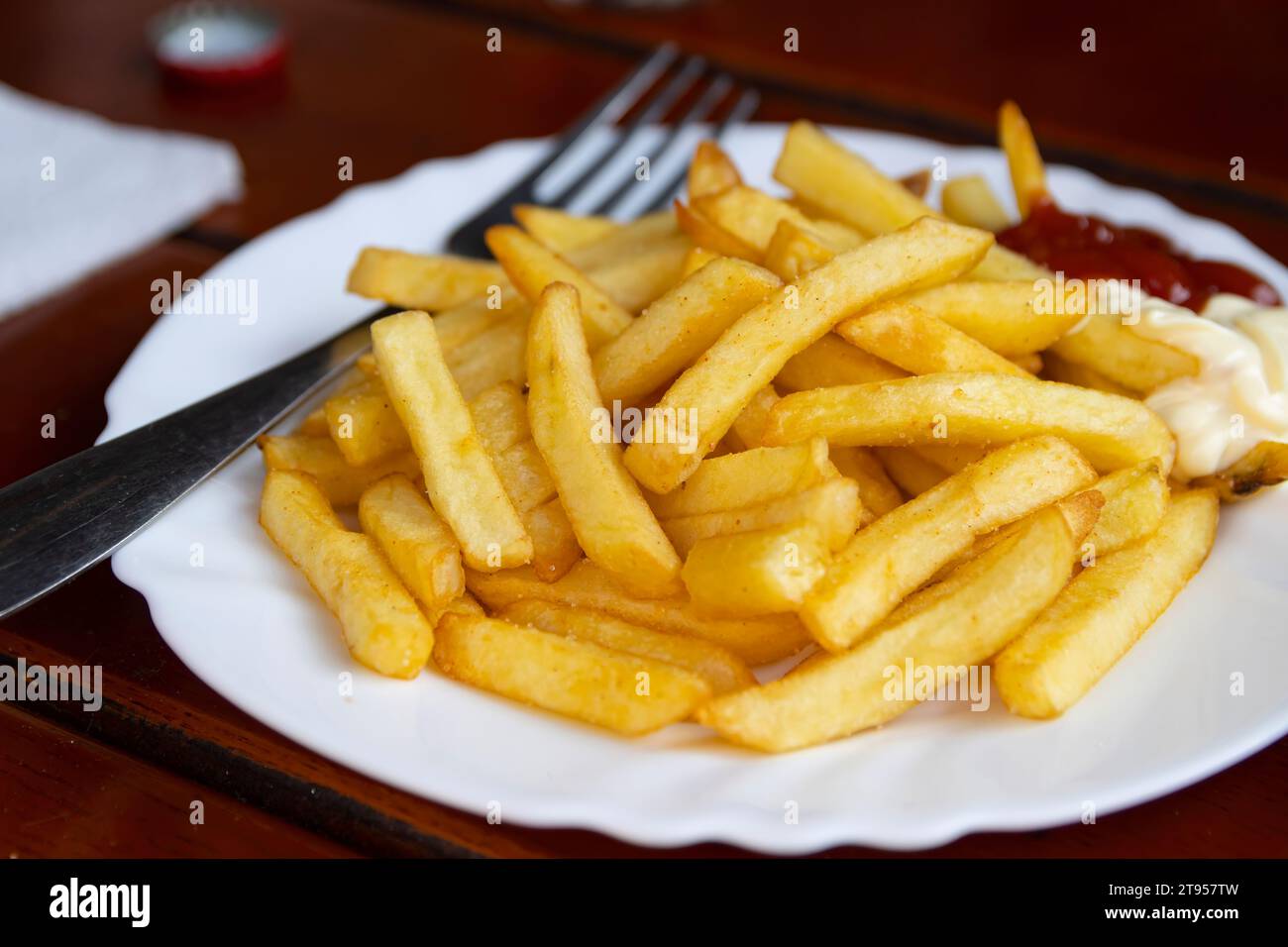 Pommes frites - chiamate anche patatine fritte o patatine fritte - servite con ketchup e condimenti di maionese a lato. Foto Stock