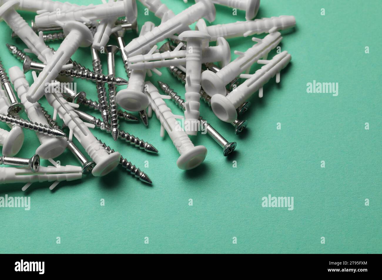 Molte viti metalliche e tasselli bianchi su sfondo turchese, primo piano Foto Stock