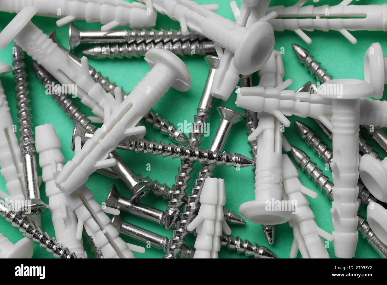 Molte viti metalliche e tasselli bianchi su sfondo turchese, primo piano Foto Stock