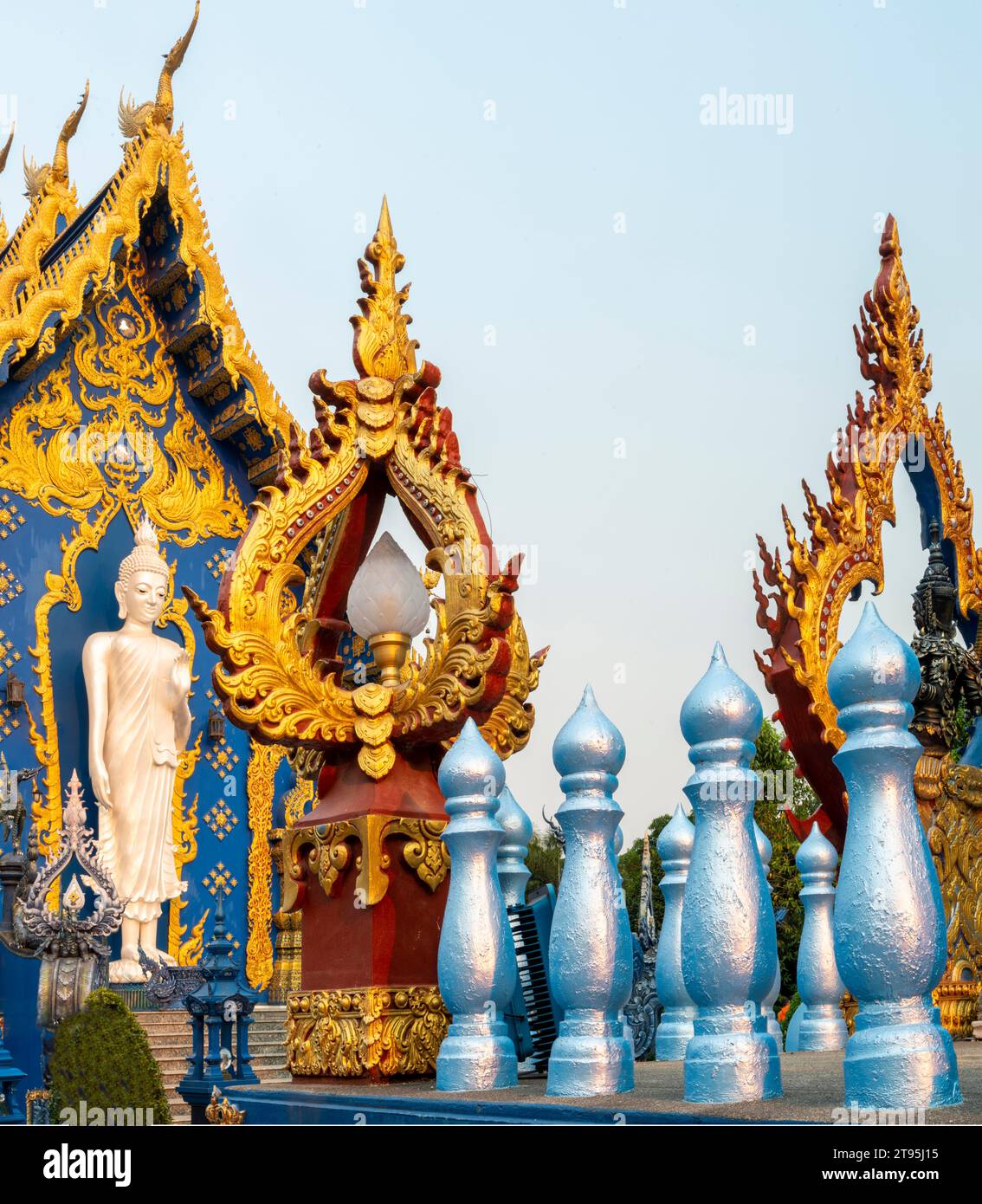 Esterno, splendidamente decorato con disegni blu e oro, statua di Buddha bianco-argento accanto all'ingresso del tempio e calda luce del tramonto che splende Foto Stock