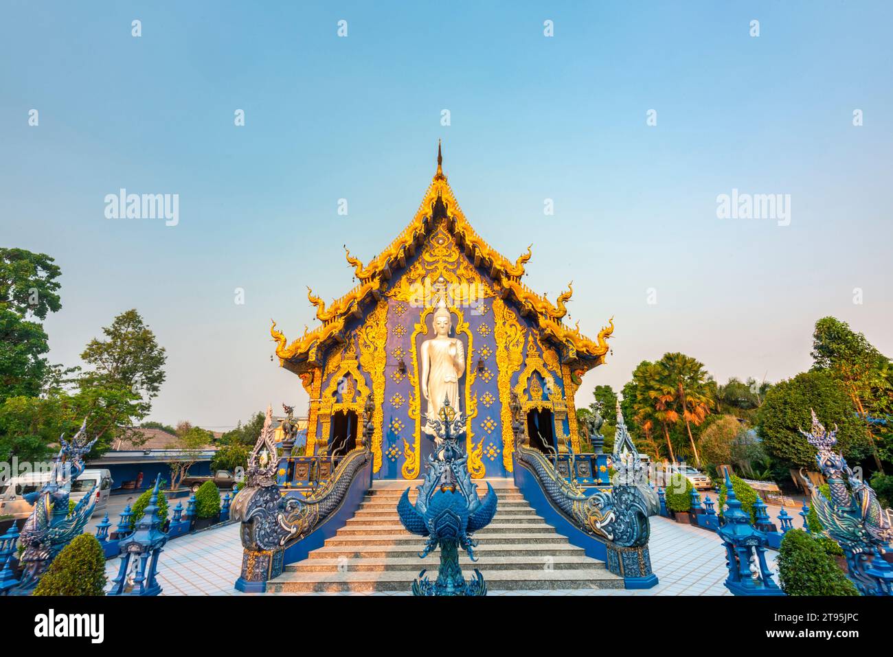 Splendidamente decorata con disegni blu e oro, una grande statua di Buddha bianco-argento in piedi accanto all'ingresso del tempio e una calda luce del tramonto che splende Foto Stock