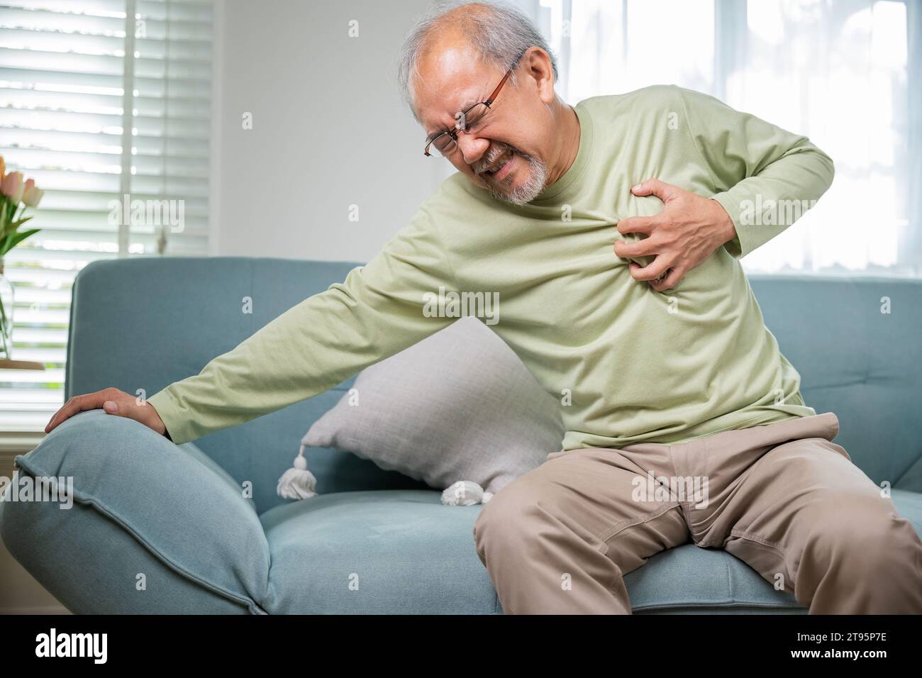 Un uomo anziano triste che sente dolore usa la mano toccando il petto avendo un attacco di cuore Foto Stock