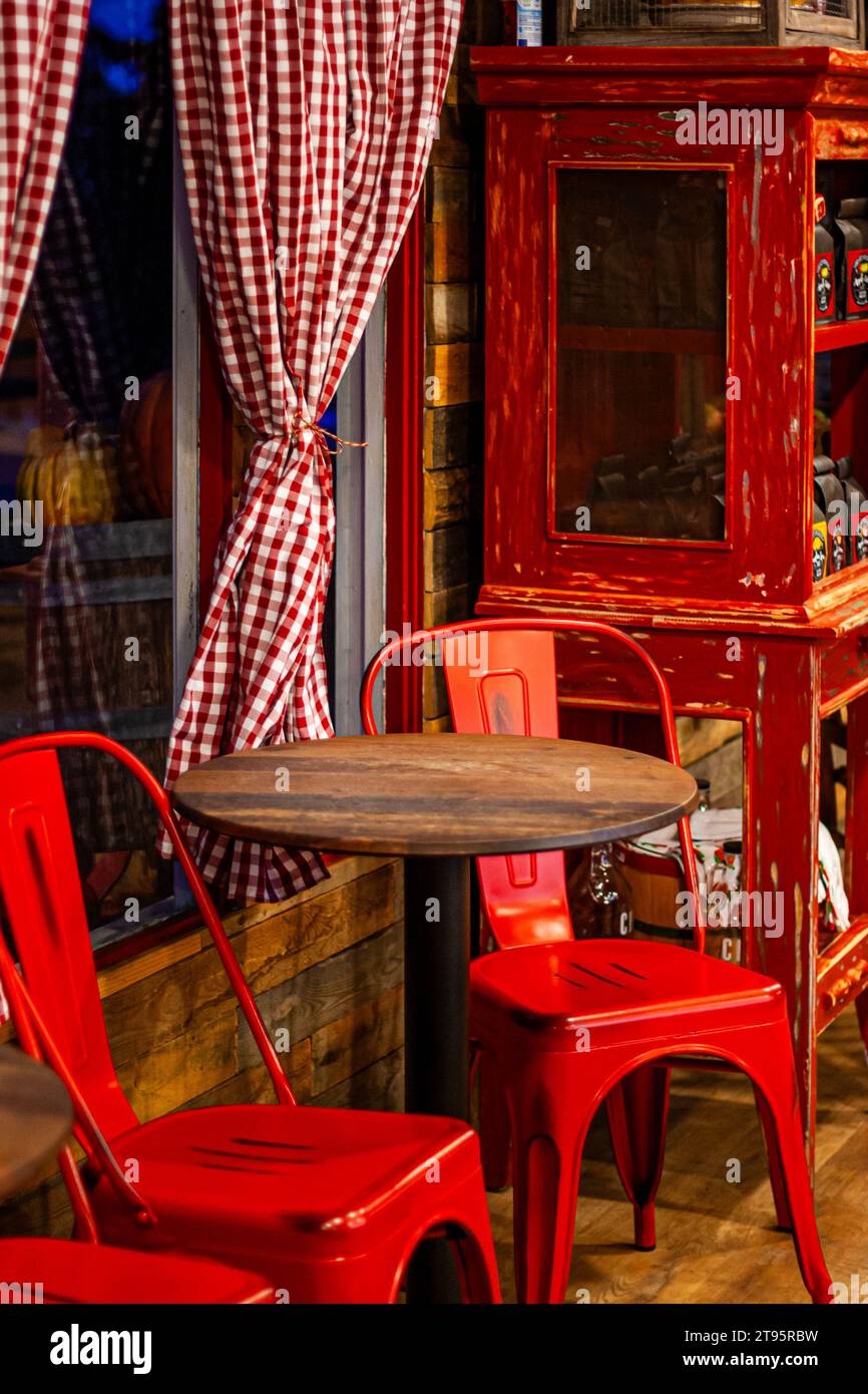 Sedie rosse ai tavoli di legno in un negozio con tende a Vichy rosse e bianche sulle finestre Foto Stock