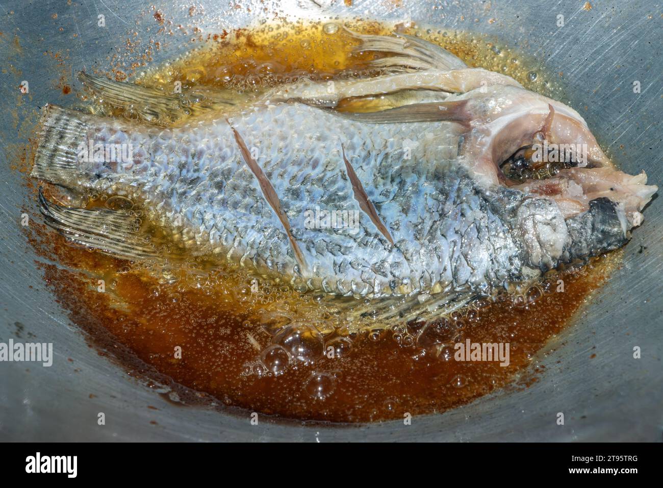 Il pesce tilapia viene fritto in olio in una padella, vista dall'alto Foto Stock