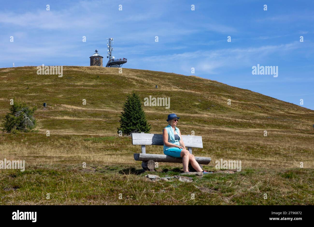 Escursionista seduto su una panchina sul Gerlitzen con vista sul Kanzelhoehe, sull'Alpe Gerlitzen, sul Nockberge, sul Gurktaler Alpen, sulla Carinzia, Austria Foto Stock