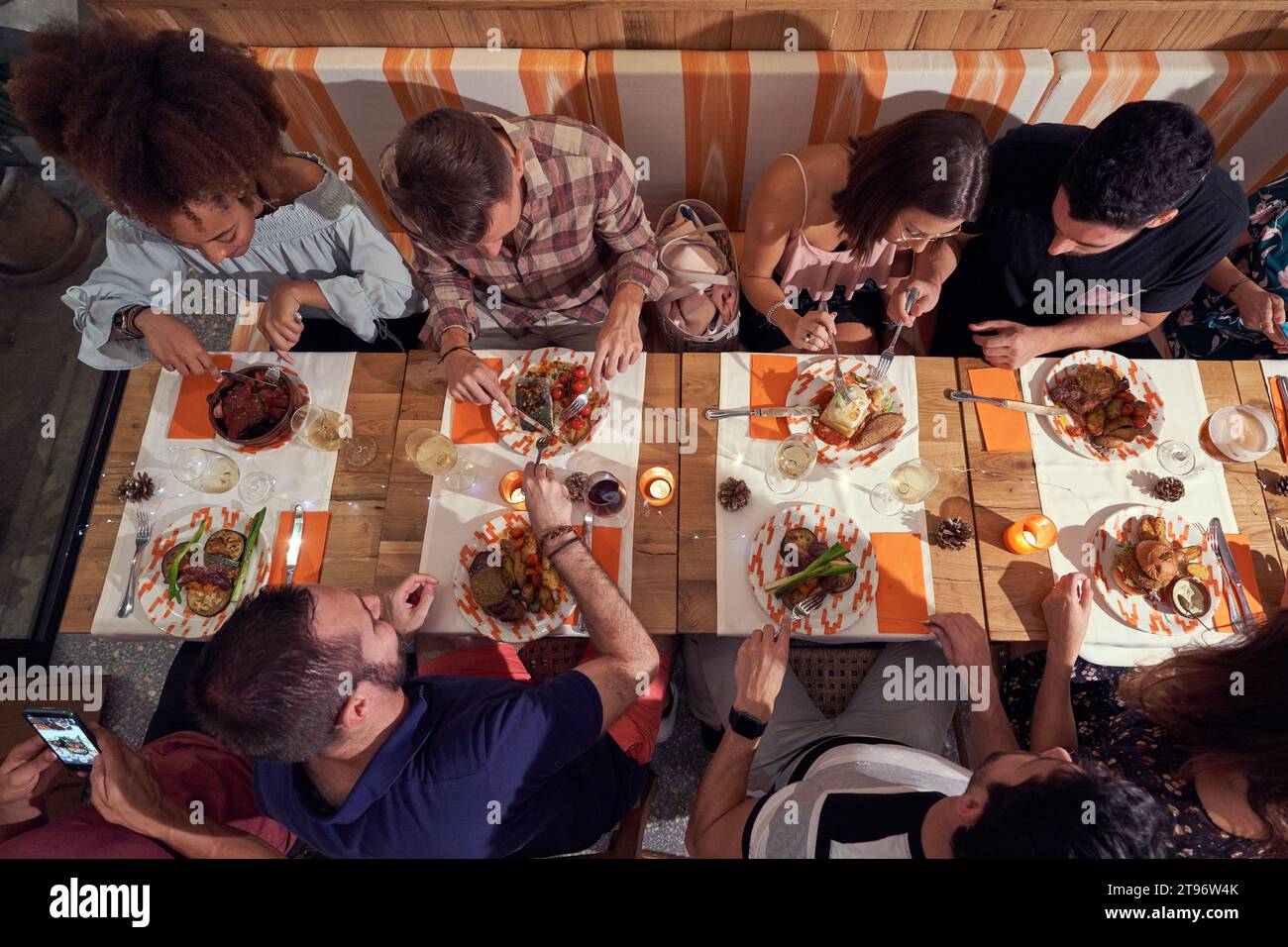 Dall'alto gruppo di amici multietnici seduti a tavola con vari piatti e bevande alcoliche mentre cenano insieme nel ristorante Foto Stock