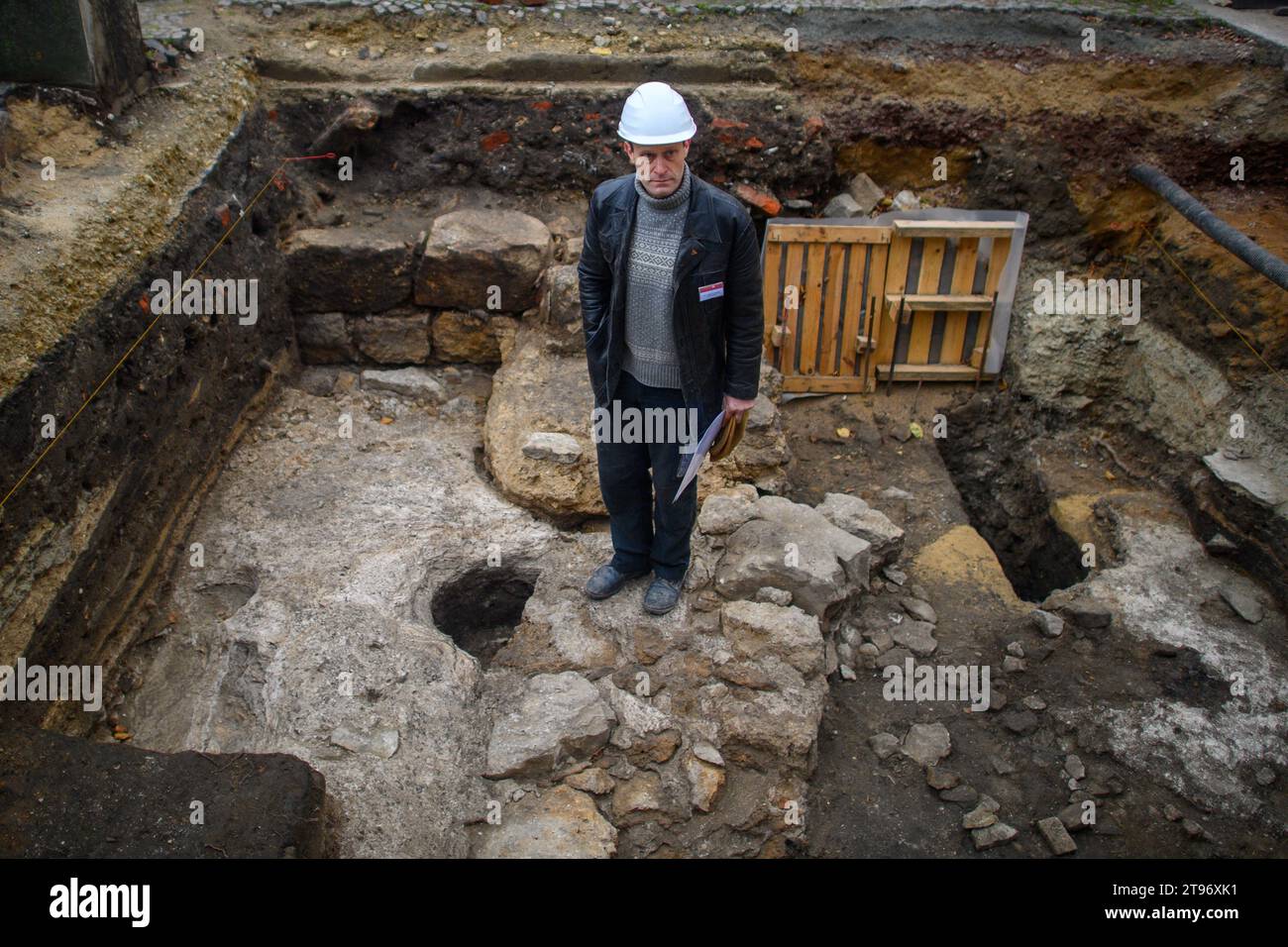 23 novembre 2023, Sassonia-Anhalt, Magdeburgo: Holger Grönwald, archeologo e direttore degli scavi dell'Ufficio statale Sassonia-Anhalt per la conservazione dei monumenti e l'archeologia, si trova sui resti di un muro in una fossa di scavo. La piazza della cattedrale di Magdeburgo è stata oggetto di diverse indagini archeologiche negli ultimi decenni. Ora, per la prima volta, i ricercatori hanno scoperto resti di muri in cemento risalenti a circa 1000 anni fa, ai tempi dei governanti ottoniani. I resti provengono dalla parete esterna di una stanza semicircolare, una cosiddetta abside, così come una base murale. Magdeb Foto Stock