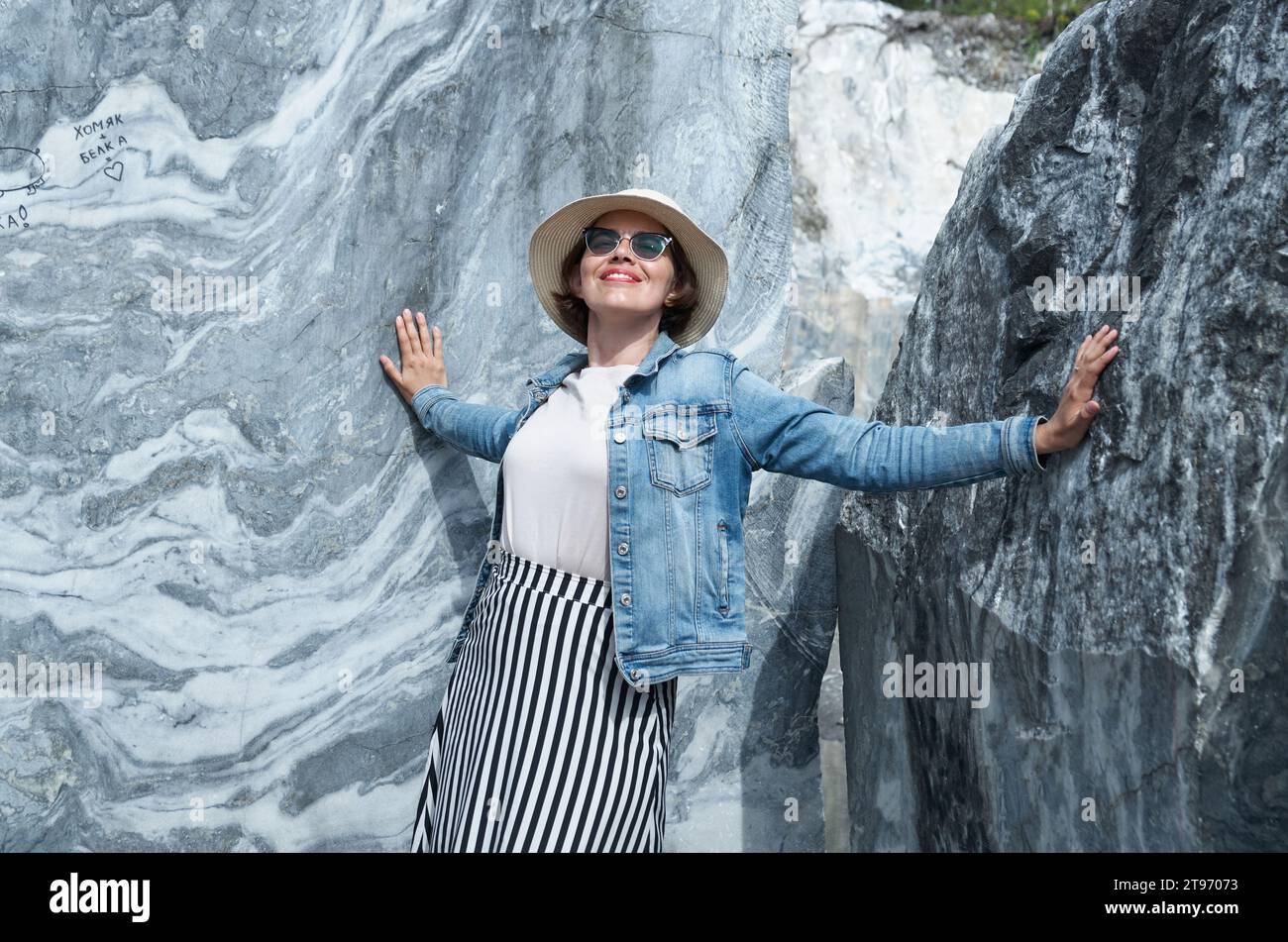 Una turista femminile con un cappello di paglia e una giacca in denim si pone sullo sfondo di una parete in marmo naturale Foto Stock