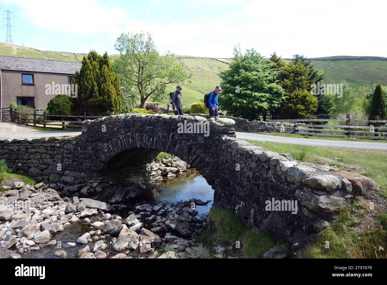 Two Men (escursionisti) Crossing a Pack Horse Bridge a Hause Foot nella Crookdale Valley nel Lake District National Park, Cumbria, Inghilterra, Regno Unito Foto Stock