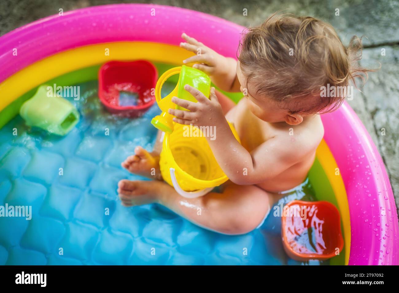 Bambino seduto in una piscina in giardino e che gioca con i giochi d'acqua. Calda giornata estiva nella natura Foto Stock