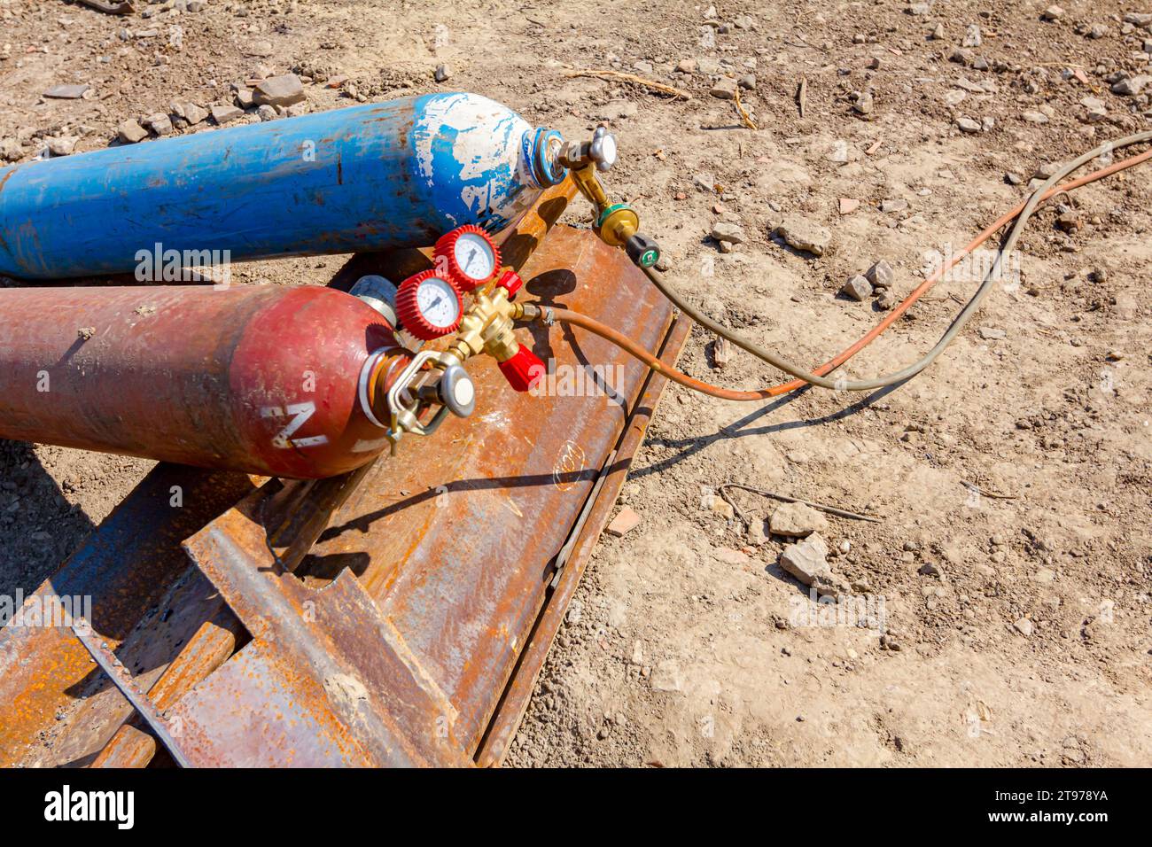 Apparecchiature di saldatura rosse e blu, serbatoi di ossigeno e azoto con valvole e manometri, bombole di gas acetilene posizionate su pali metallici all'interno della struttura Foto Stock