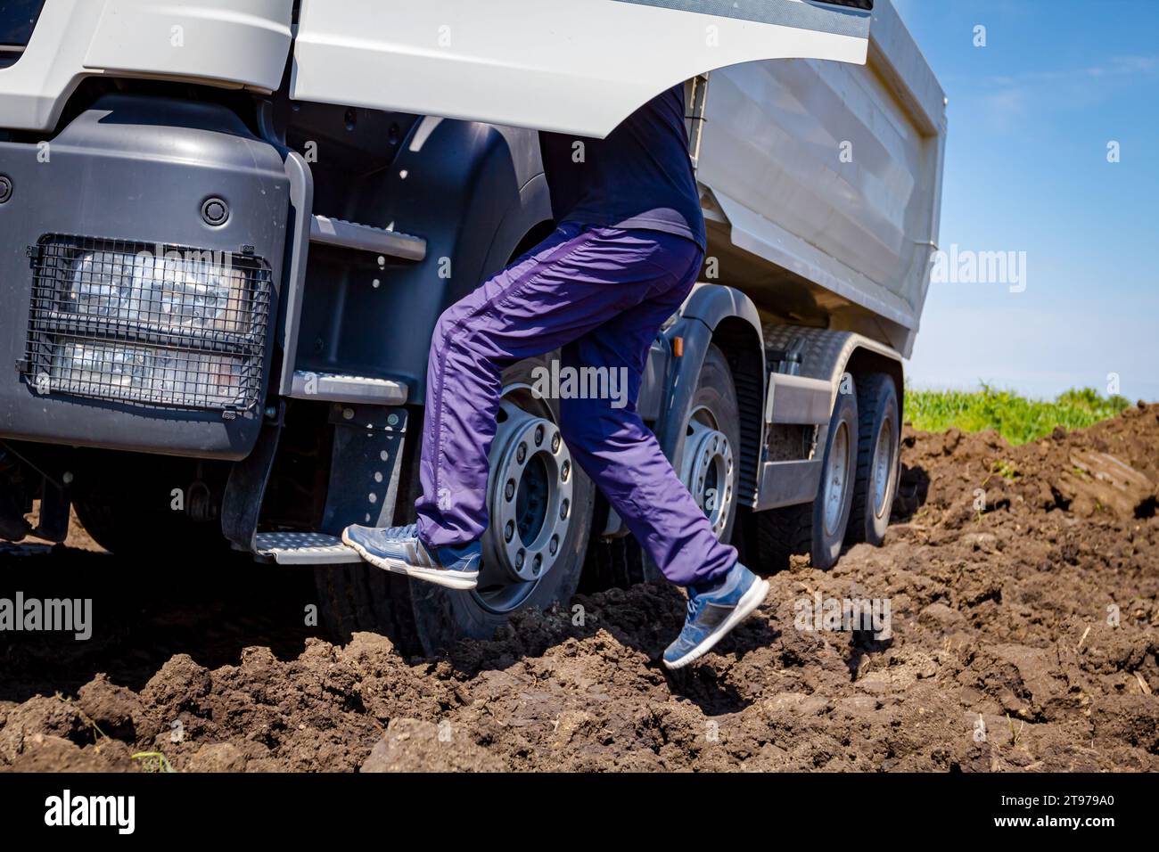 Vista dall'angolo basso sul lato anteriore del veicolo, il conducente sta salendo in cabina, l'autocarro parcheggiato nel cantiere. Foto Stock