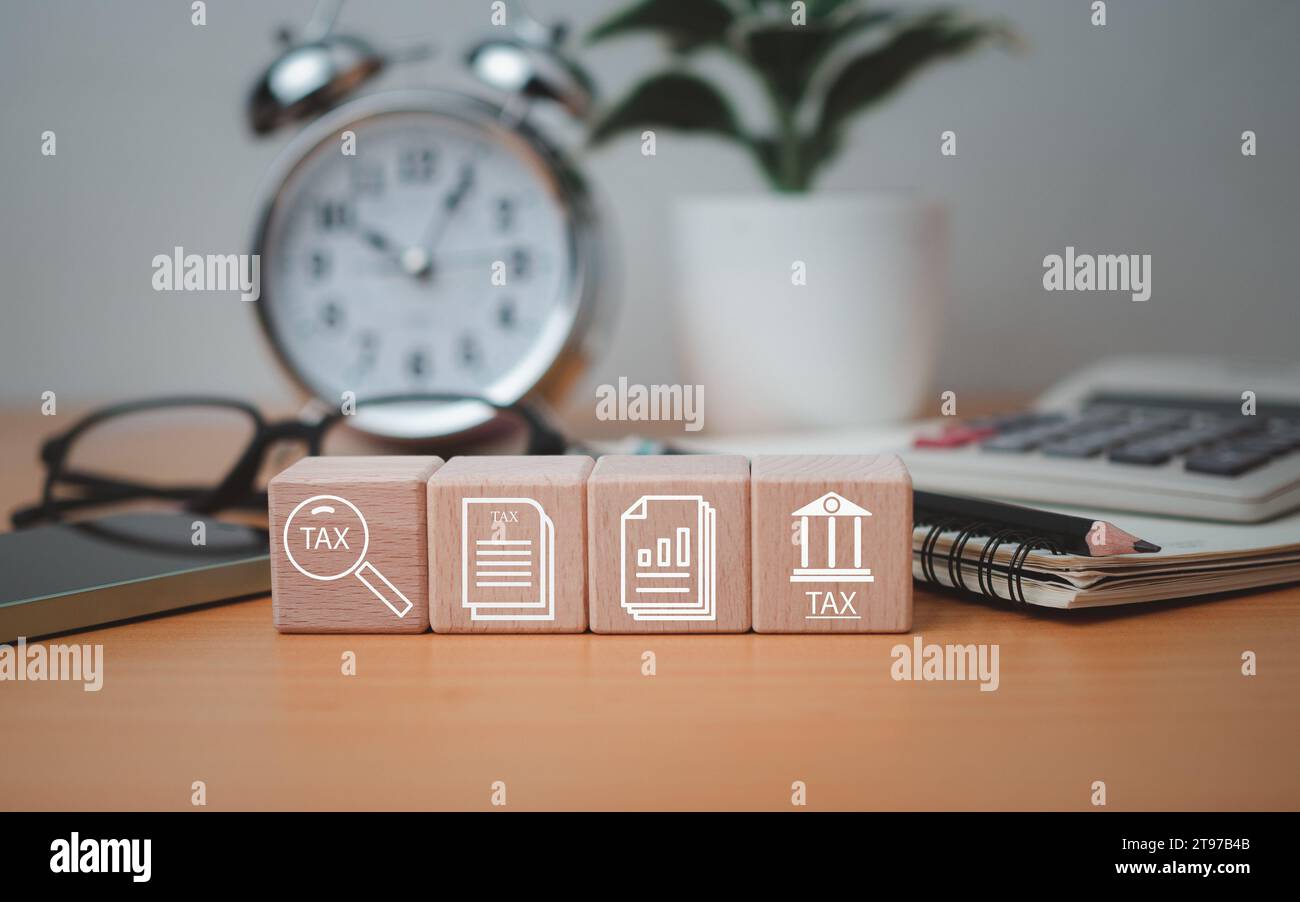 Icone di simboli fiscali stampati a blocchi in legno posizionate su un piano in legno con forniture per ufficio, ricerche finanziarie, report, calcoli della dichiarazione dei redditi. Foto Stock