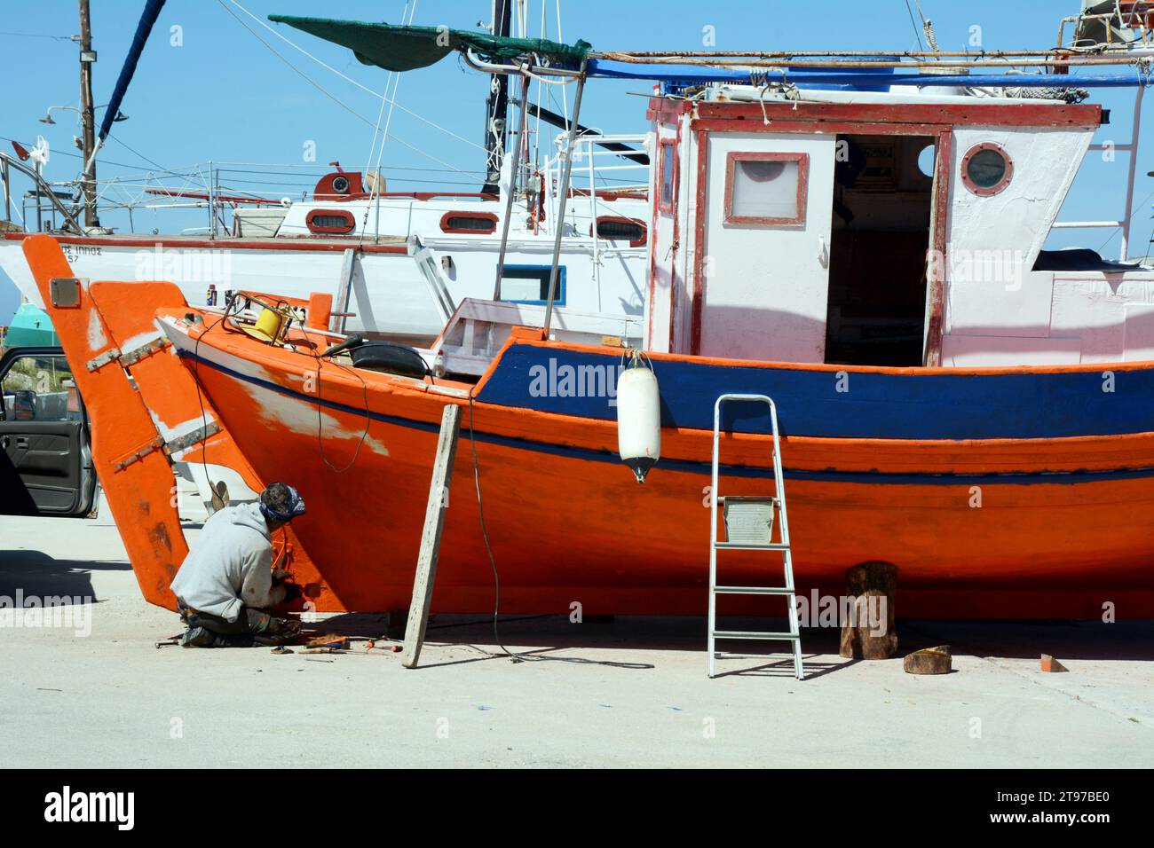 Un pescatore greco di Ikaria dipinge la sua barca nel villaggio di pescatori e nel porto di Gialiskari, sulla costa settentrionale dell'isola di Ikaria, una "zona blu" in Grecia. Foto Stock