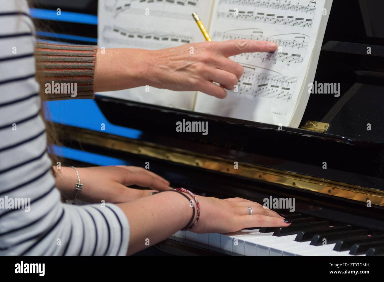 Mani umane di un insegnante di pianoforte che spiega a uno studente che suona le note chiave e gli accordi su un classico pianoforte nero durante un pianolesson Foto Stock