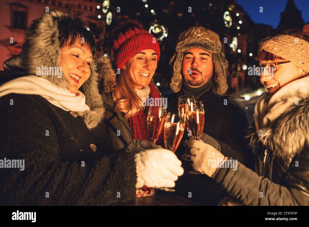 Un gruppo di amici che brinda con champagne in una serata festiva in un mercatino di natale Foto Stock
