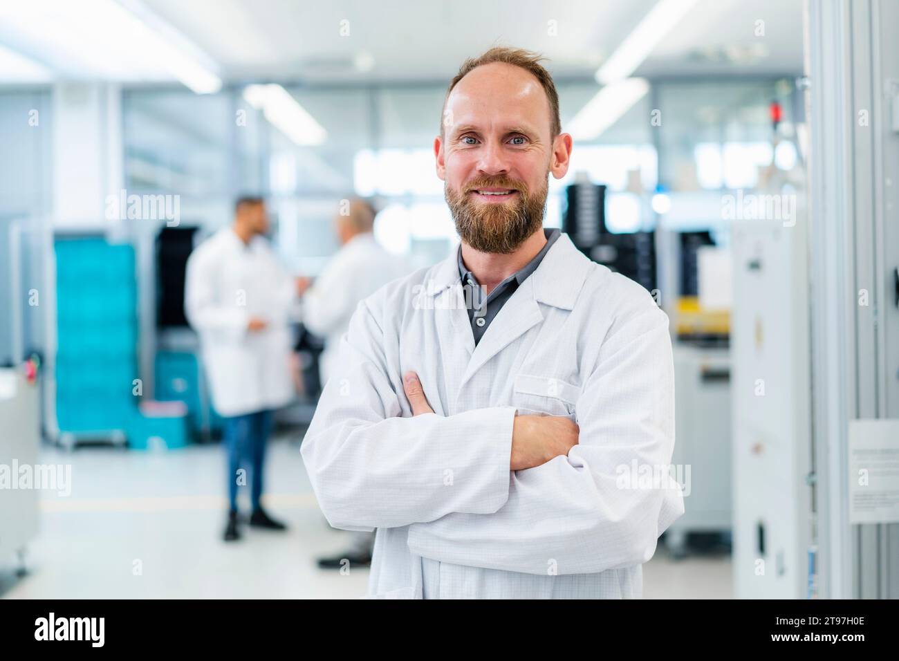 Tecnico elettrico sicuro in piedi nella fabbrica di elettronica con le braccia incrociate Foto Stock