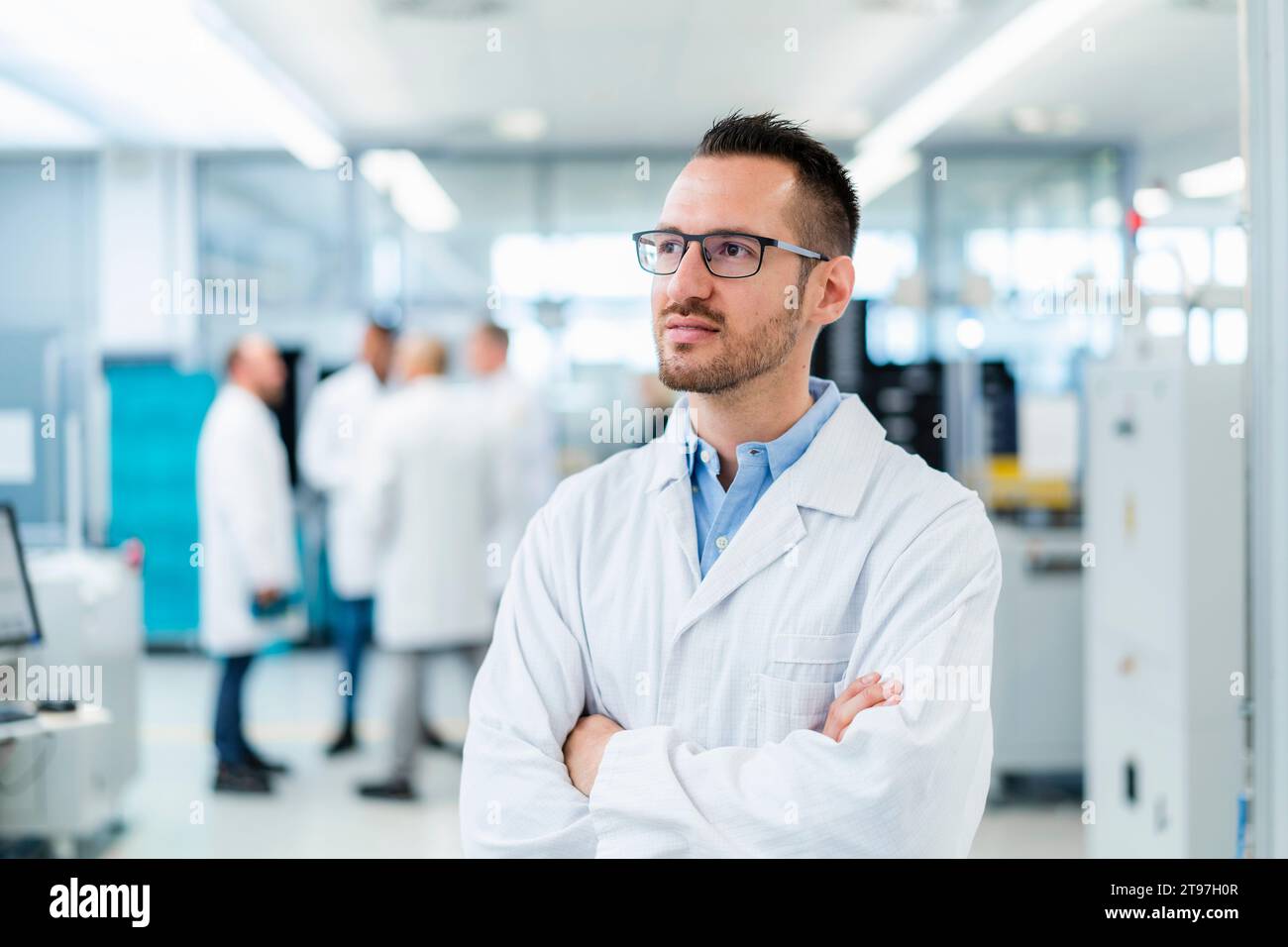 Tecnico elettrico sicuro in piedi nella fabbrica di elettronica con le braccia incrociate Foto Stock