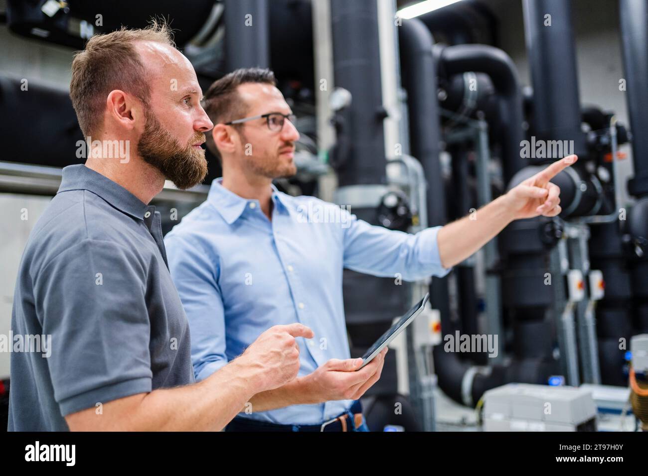 Dipendente e uomo d'affari con un tablet digitale che parla in fabbrica Foto Stock