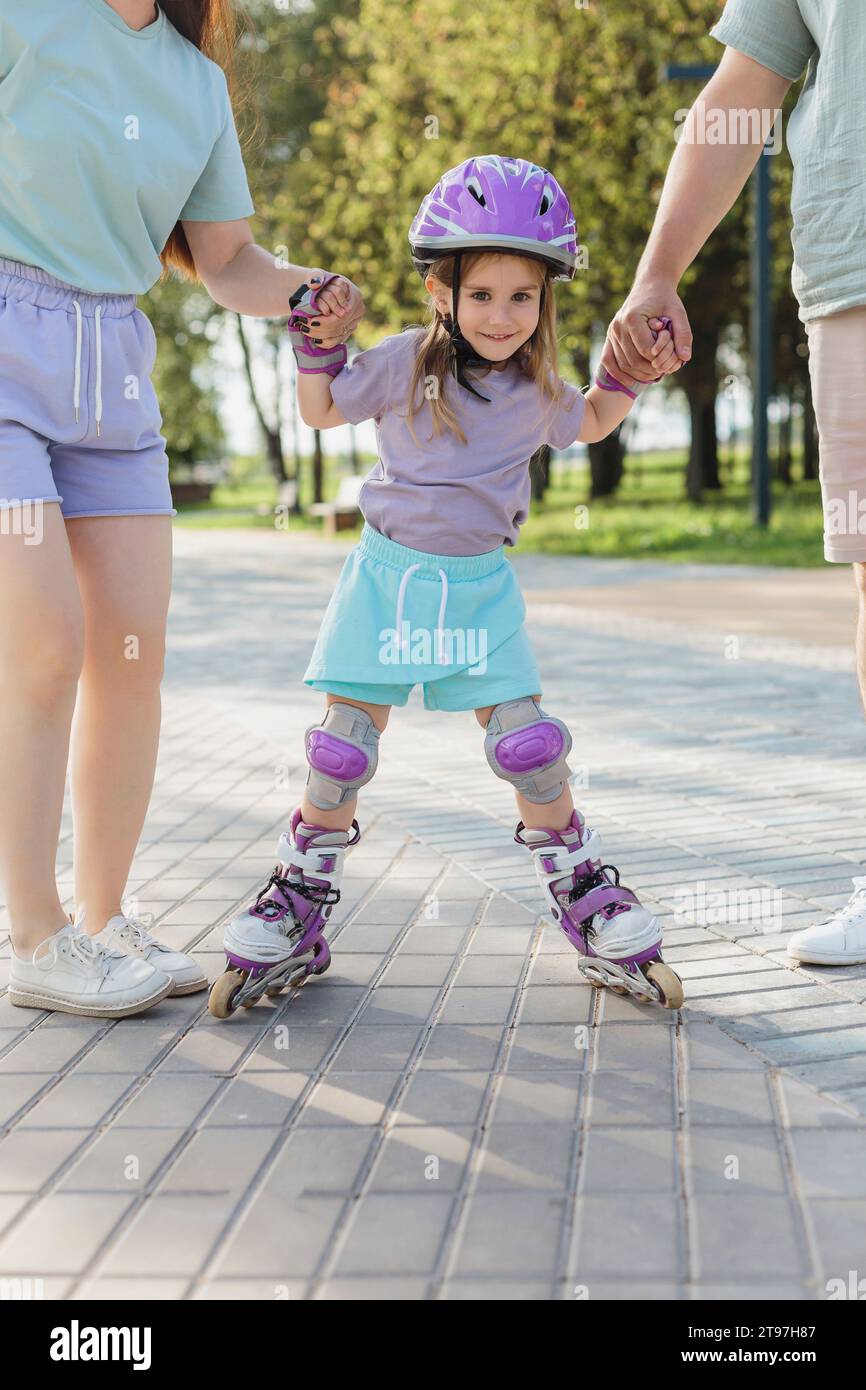 Una ragazza sorridente che pattina con i genitori sul sentiero del parco Foto Stock