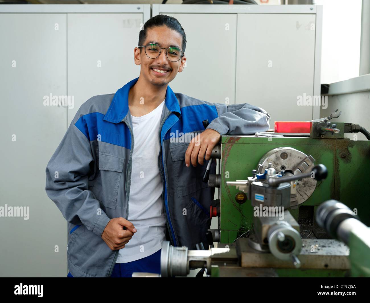 Apprendista sorridente che indossa occhiali appoggiati alla ringhiera in officina Foto Stock