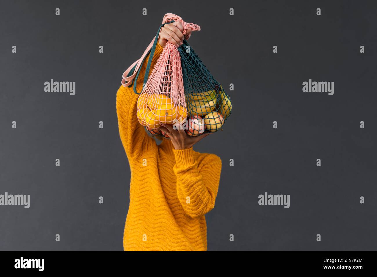 Donna che copre il viso con frutta in sacchetti in rete su sfondo nero Foto Stock