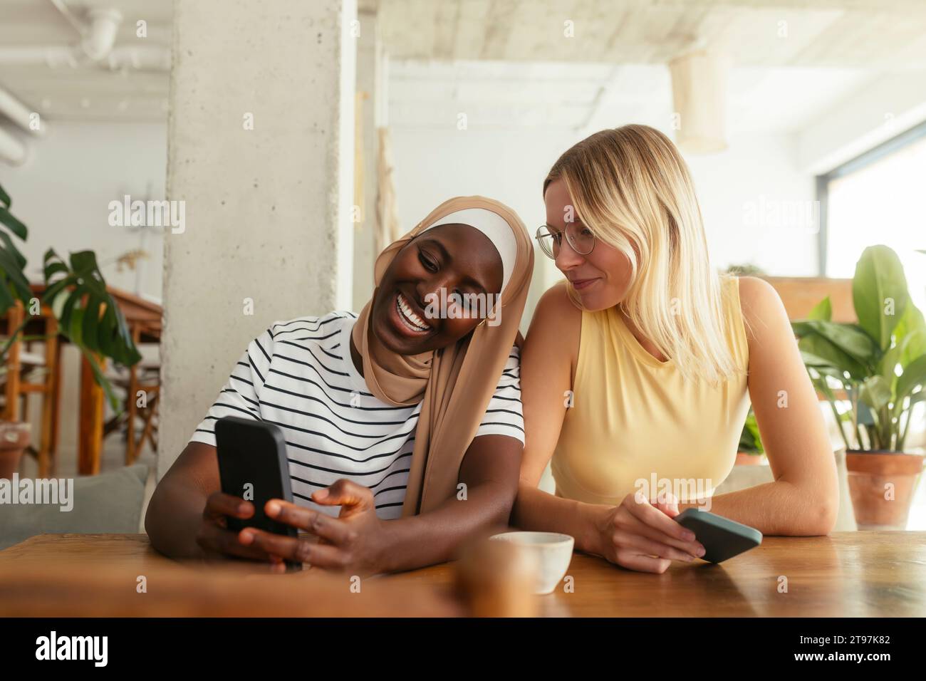 Donna sorridente che mostra lo smartphone ad un amico al bar Foto Stock