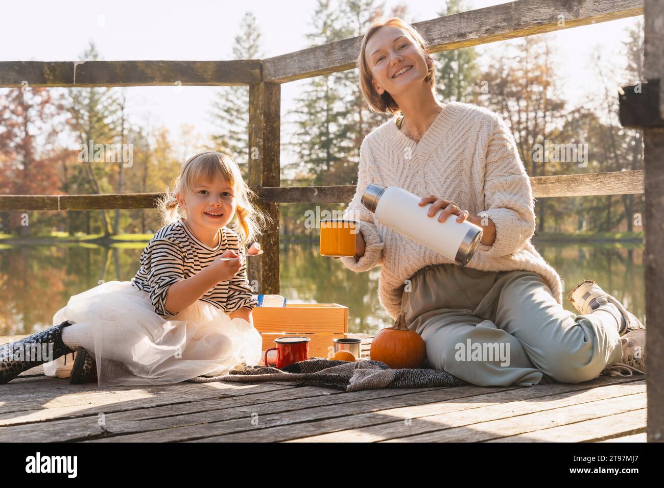 Ragazza felice con la madre che versa cioccolata calda in una tazza sulla passerella Foto Stock