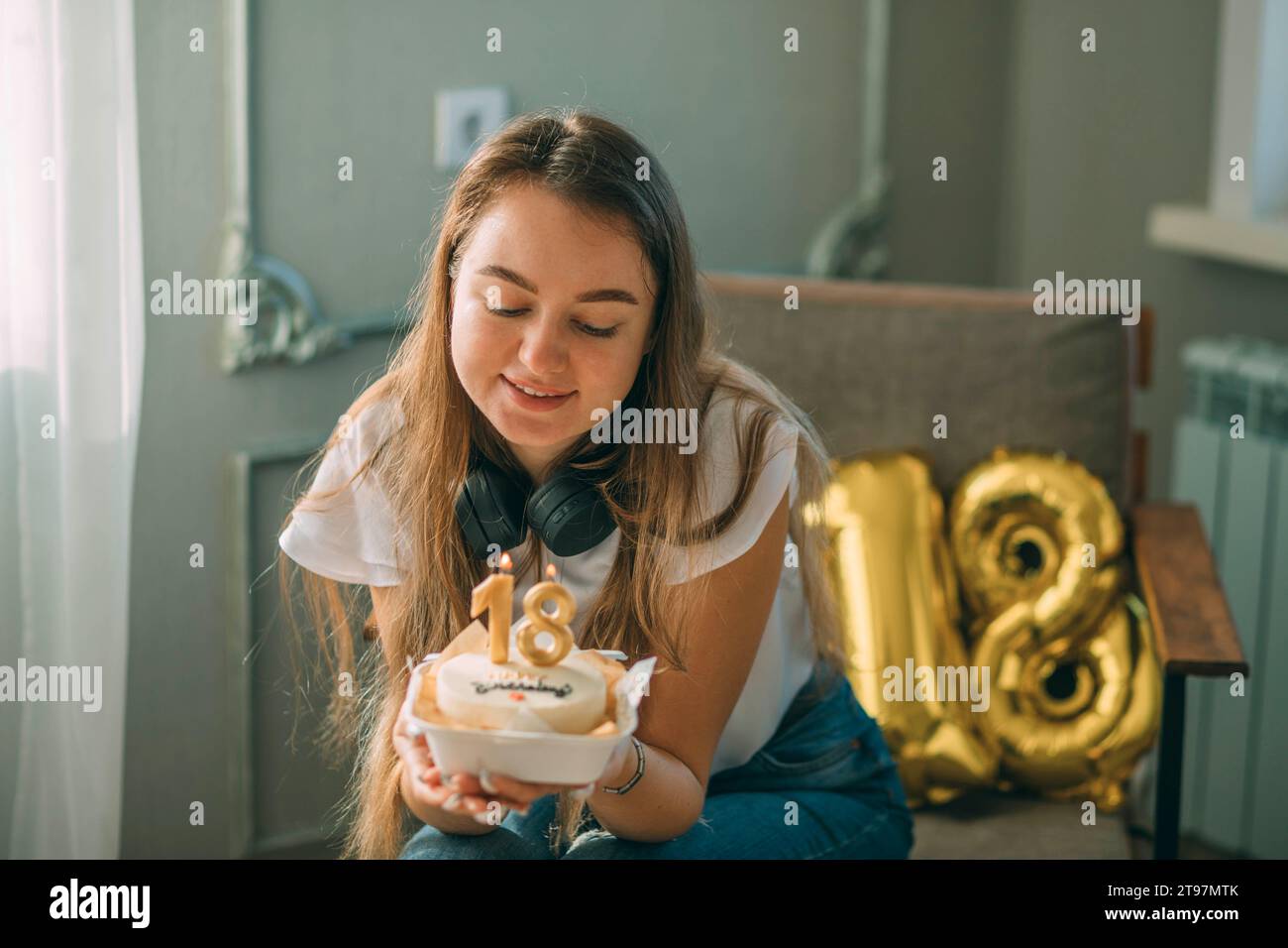 Donna sorridente che guarda la torta con le candele numero 18 per il compleanno Foto Stock