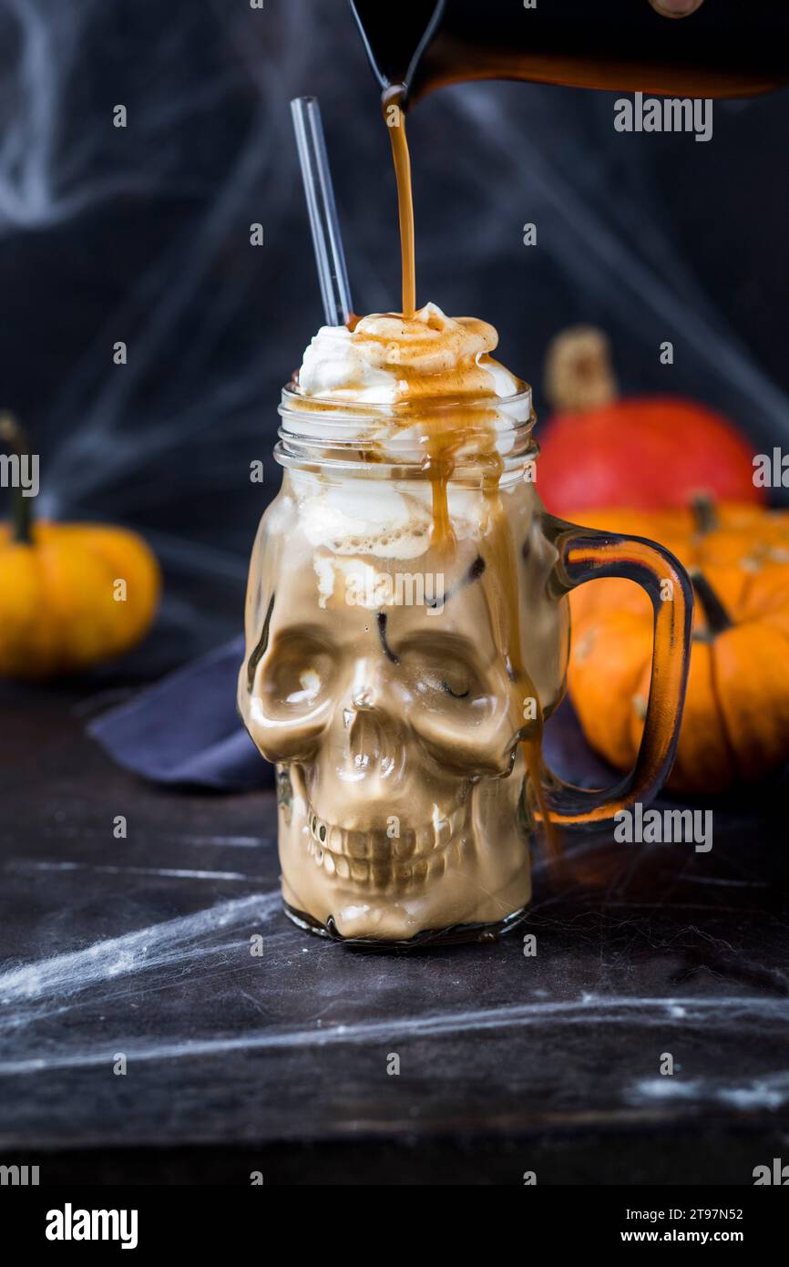 Sciroppo versato sulla tazza a forma di teschio ofÂ zucca spiceÂ latte con panna montata Foto Stock