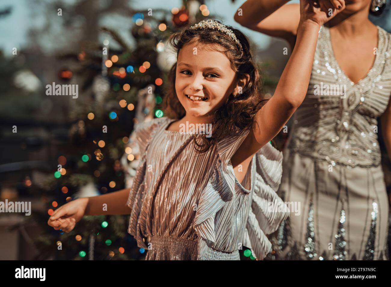 Figlia sorridente che tiene la mano della madre e balla vicino all'albero di Natale a casa Foto Stock