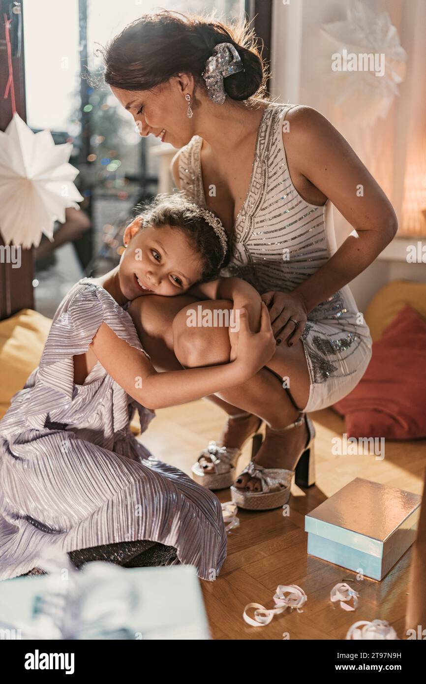 Figlia sorridente che abbraccia e si appoggia in braccio alla madre vicino al regalo di Natale a casa Foto Stock
