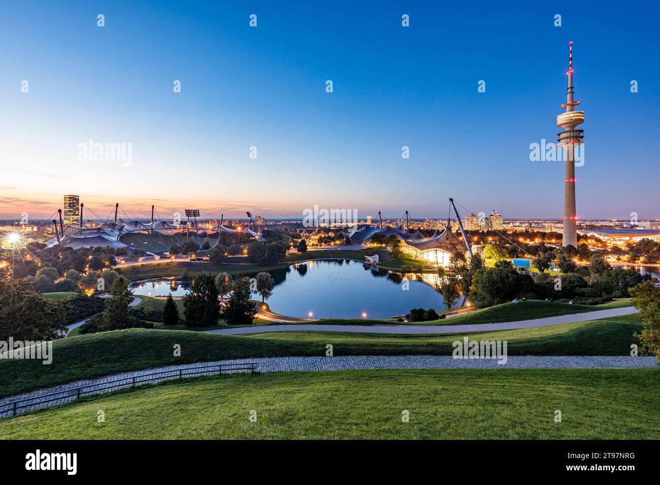 Germania, Baviera, Monaco, Parco Olimpico al tramonto con Torre Olimpica, edificio BMW e stagno sullo sfondo Foto Stock
