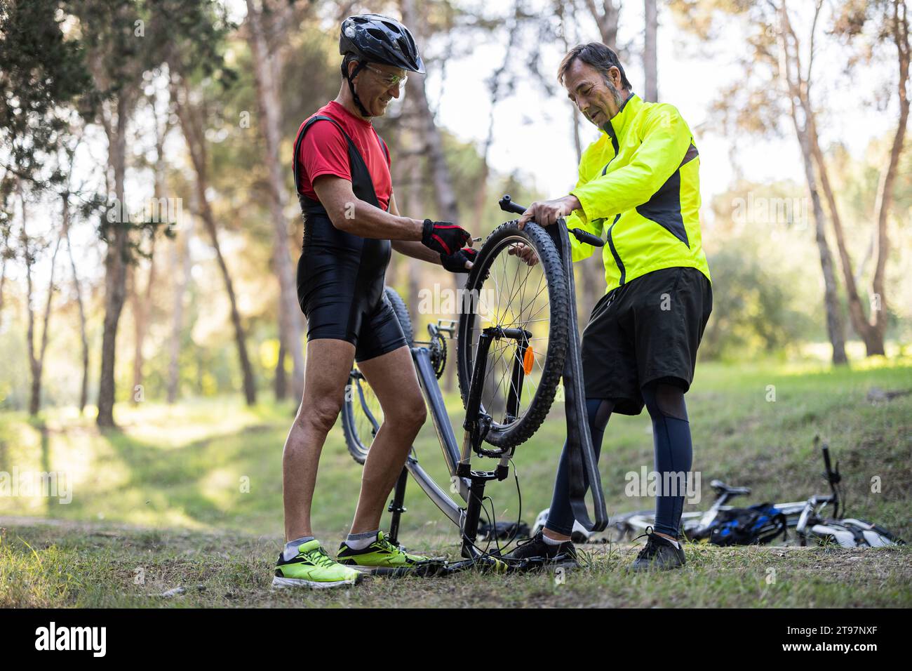 Amici maturi che riparano pneumatici di bicicletta nella foresta Foto Stock