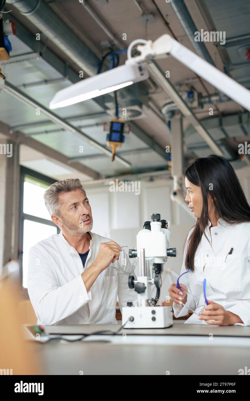 Scienziati che discutono con il microscopio alla scrivania in laboratorio Foto Stock