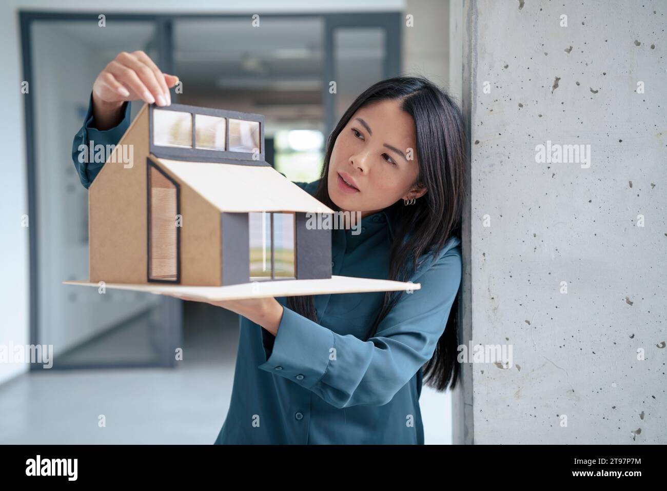 Donna d'affari che esamina la casa modello nel corridoio degli uffici Foto Stock
