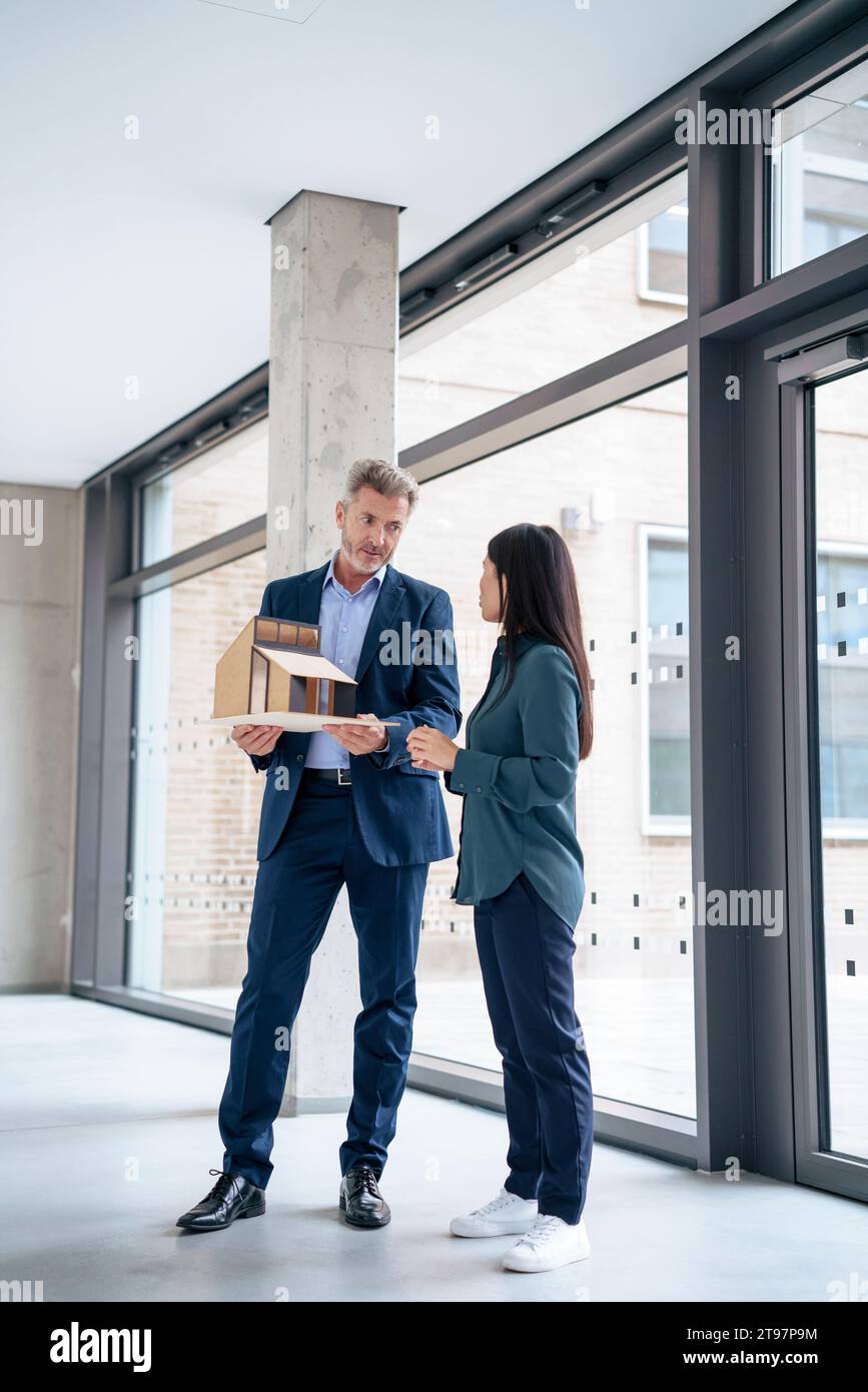 Architetto maturo che discute con un collega sulla casa modello in ufficio Foto Stock