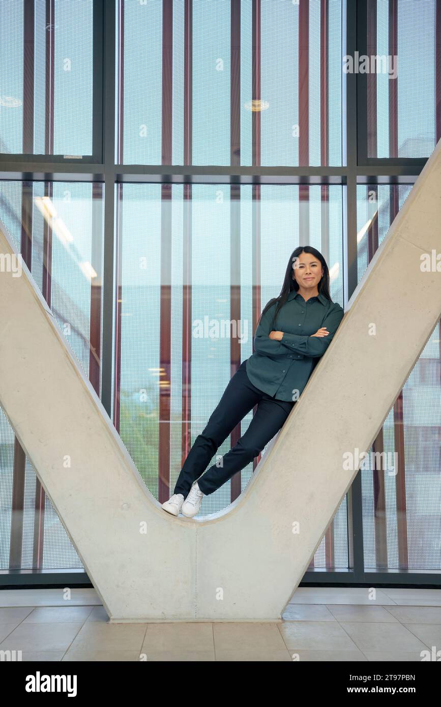 Donna d'affari sorridente con le braccia incrociate appoggiate su una colonna architettonica Foto Stock