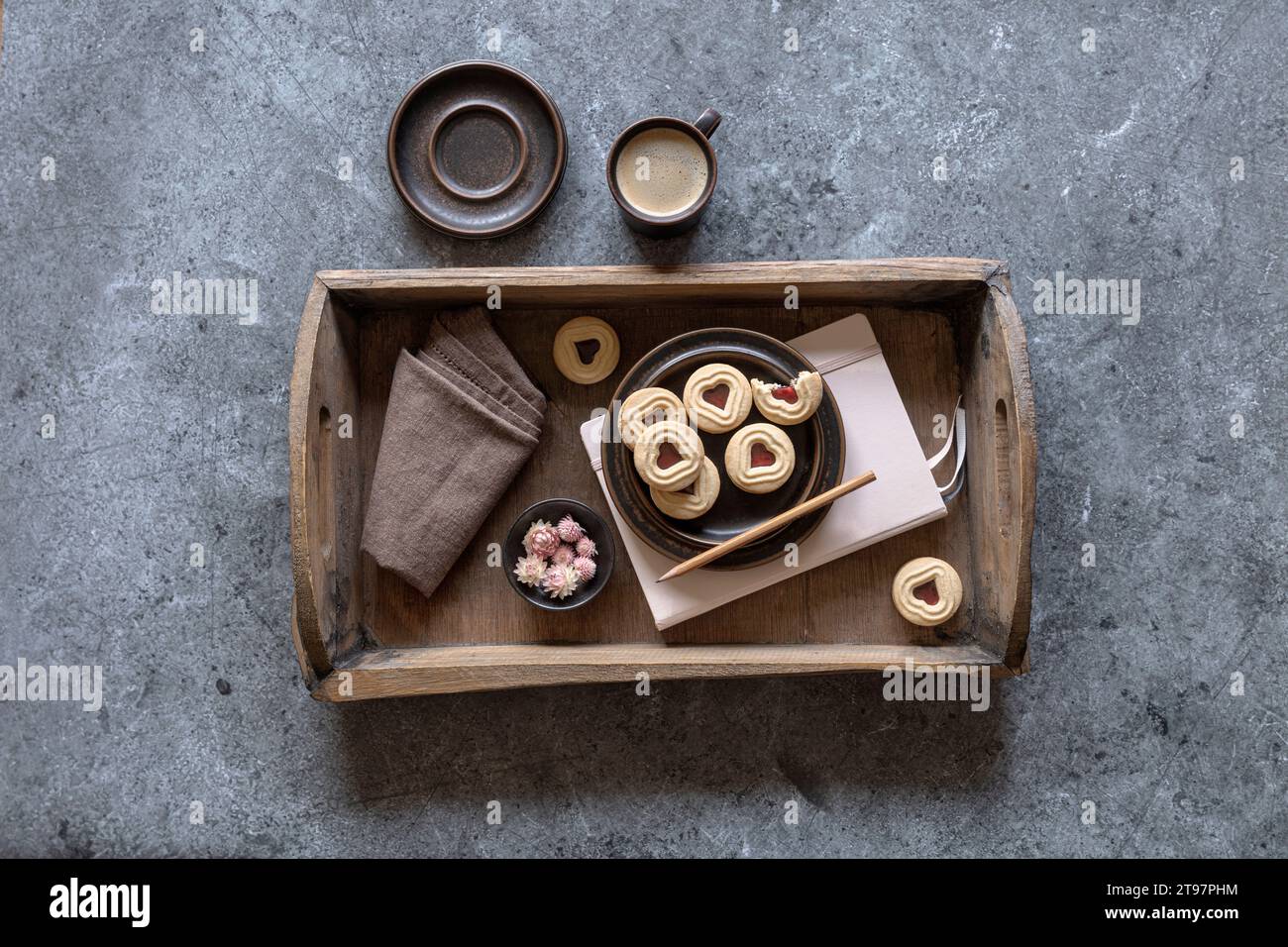 Vassoio con marmellata di biscotti, blocco note, panno per piatti, teste di fiori e tazza di caffè Foto Stock