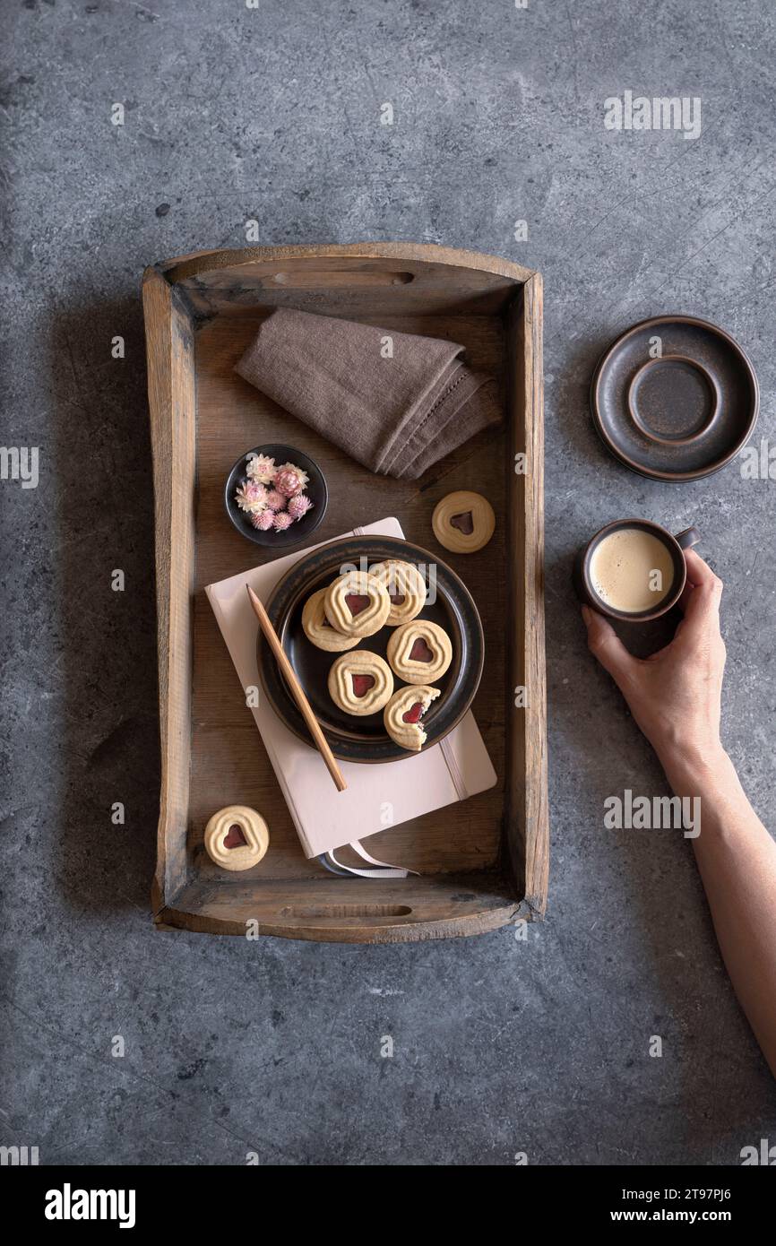 Vassoio con marmellata di biscotti, blocco note, panno per piatti, teste di fiori e tazza di caffè Foto Stock