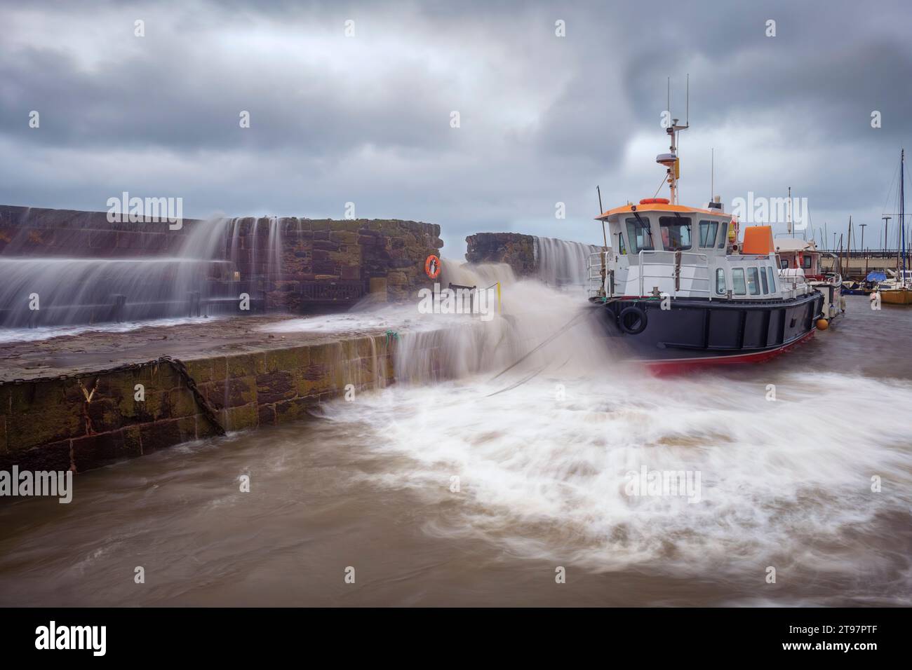 Regno Unito, Scozia, North Berwick, lunga esposizione di onde che si infrangono sul muro del porto di fronte alla barca ormeggiata Foto Stock